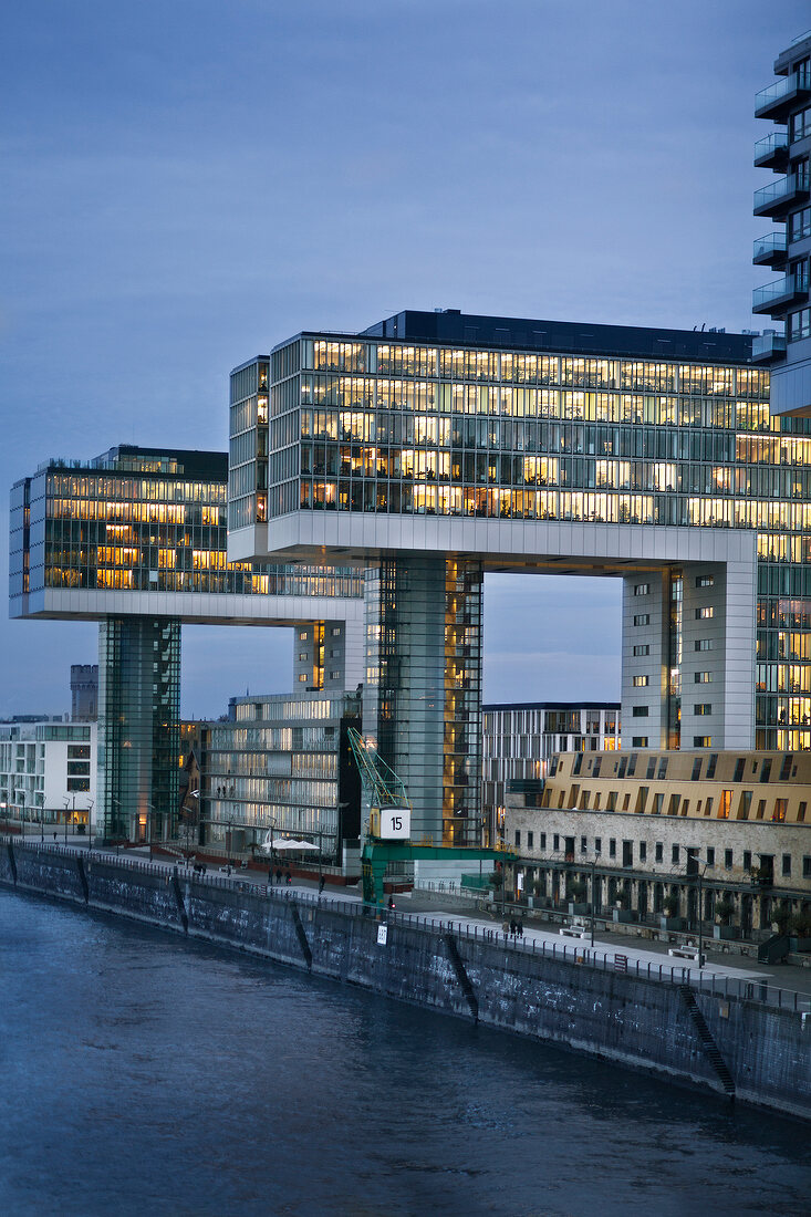 View of illuminated glass building with river at side in Rheinauhafen, Cologne, Germany