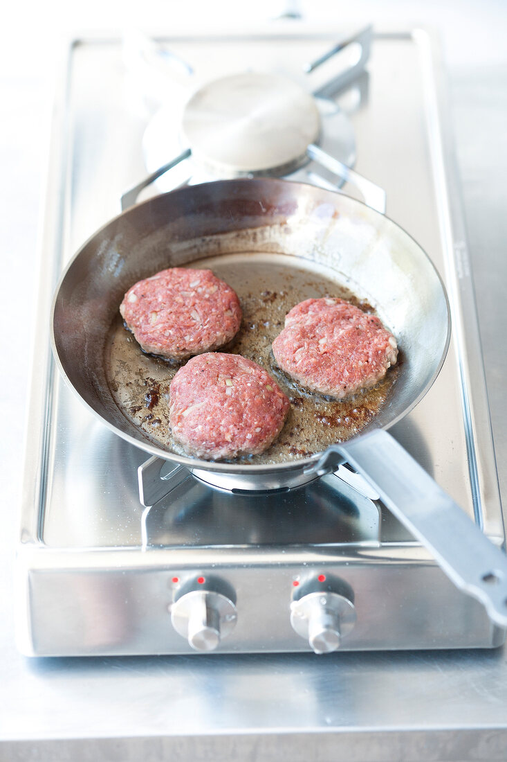 Hackfleisch, drei Frikadellen werden in einer Pfanne gebraten