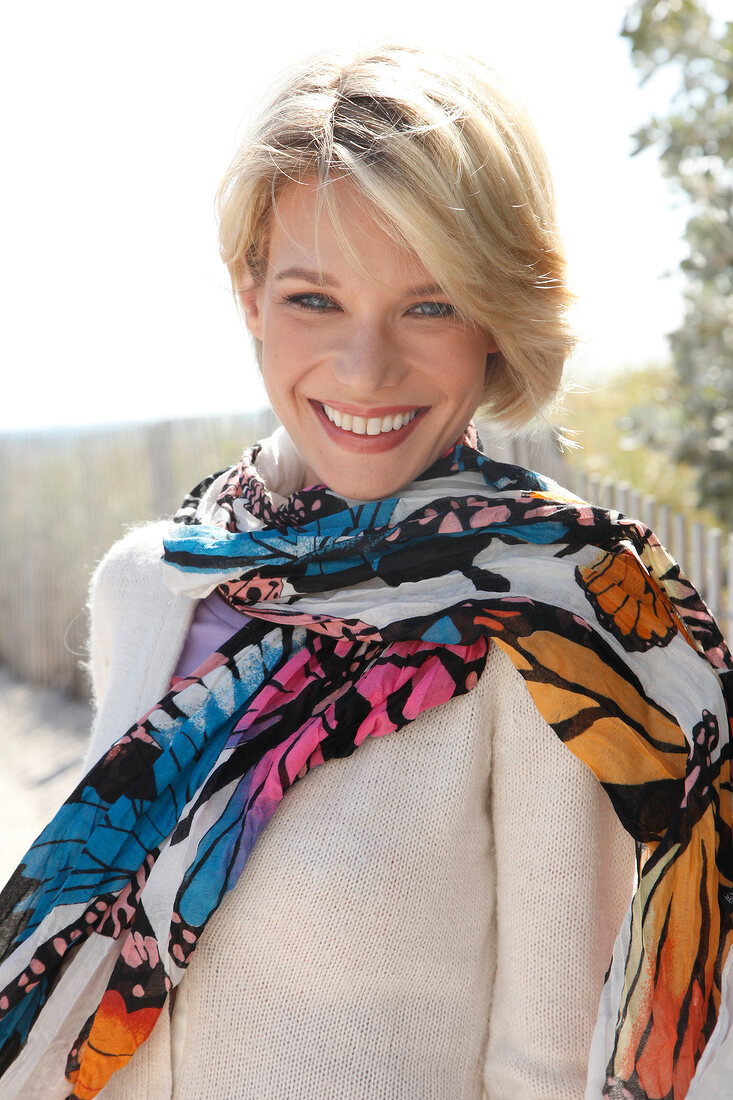 Portrait of beautiful blonde woman wearing white sweater and colourful scarf, smiling