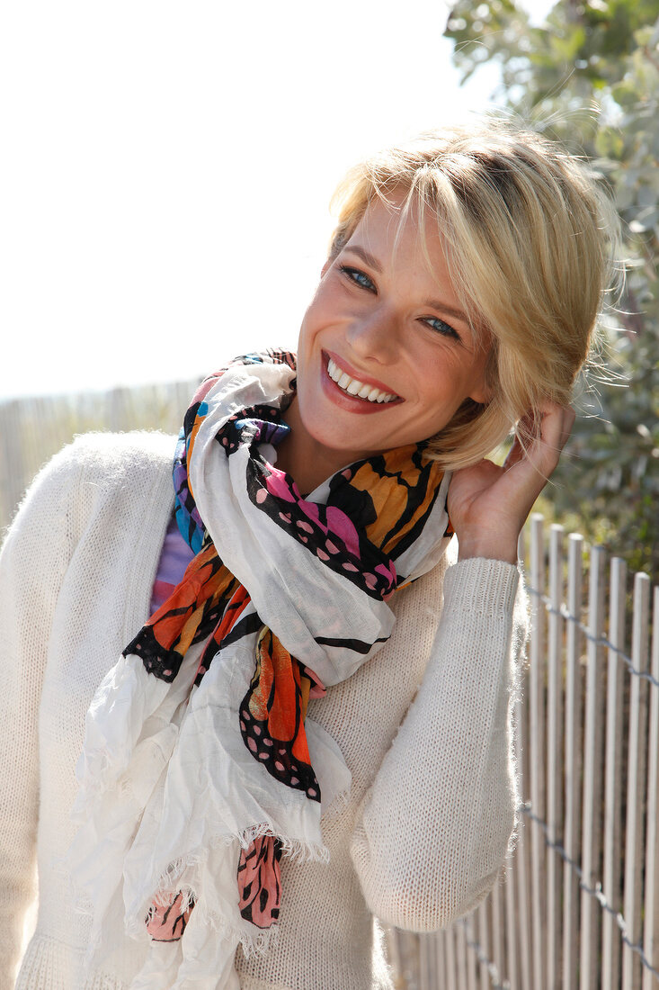 Portrait of beautiful blonde woman wearing white sweater and colourful scarf, smiling