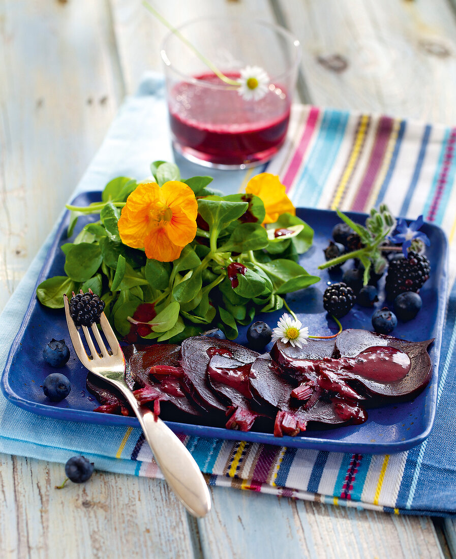 Corn salad with beetroot, berries and nasturtium on blue plate