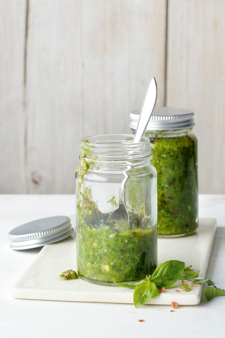 Glass jars of basil and bacon paste on cutting board