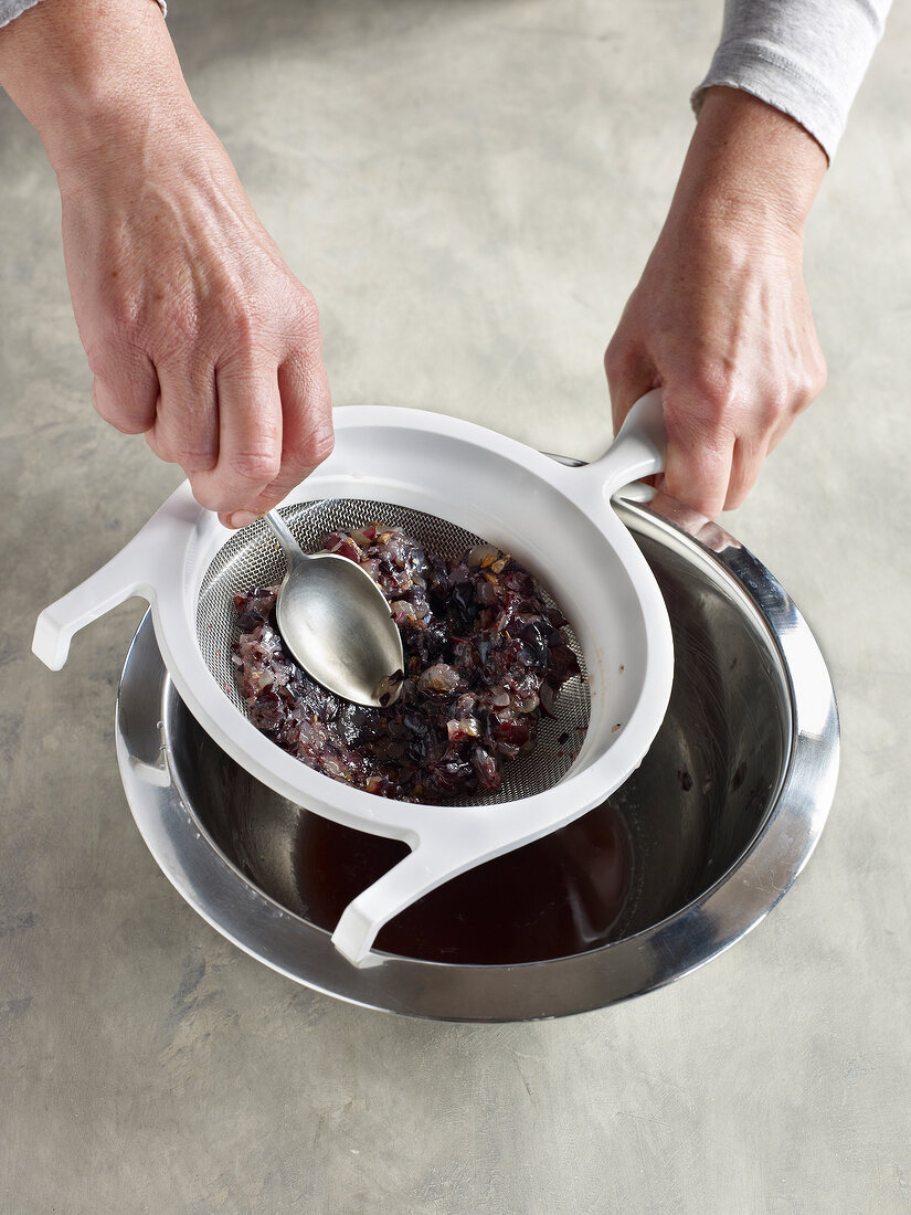 Close-up of straining blue grapes through sieve in metal bowl