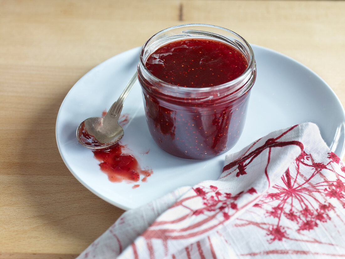 Confiture jam jar with spoon and tea towel on plate