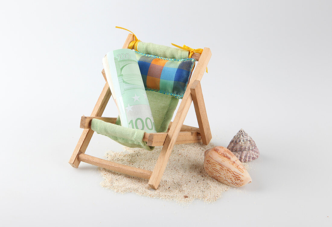 Rolled bill on deck chair, shells and sand on white background
