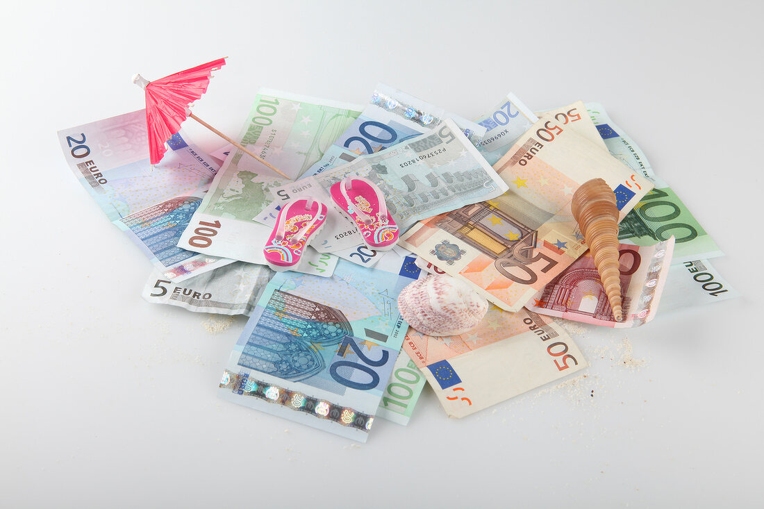 Heap of bills, umbrella, flip-flops and shells on white background