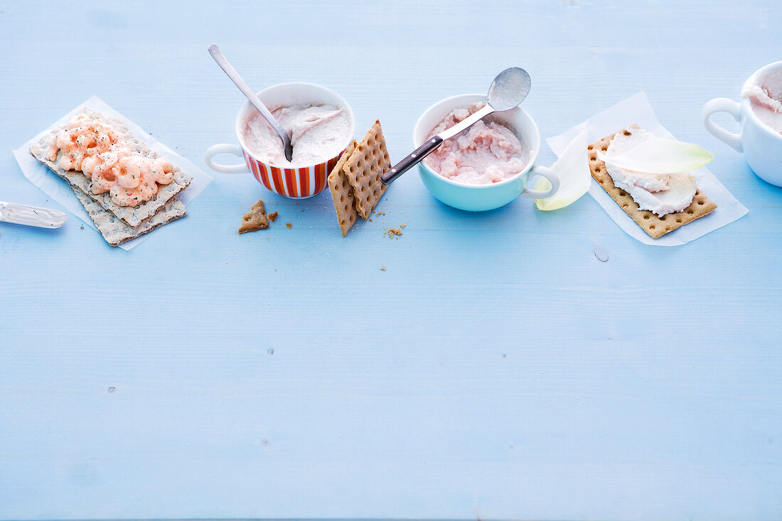 Spreads in cup and crisp breads on blue background