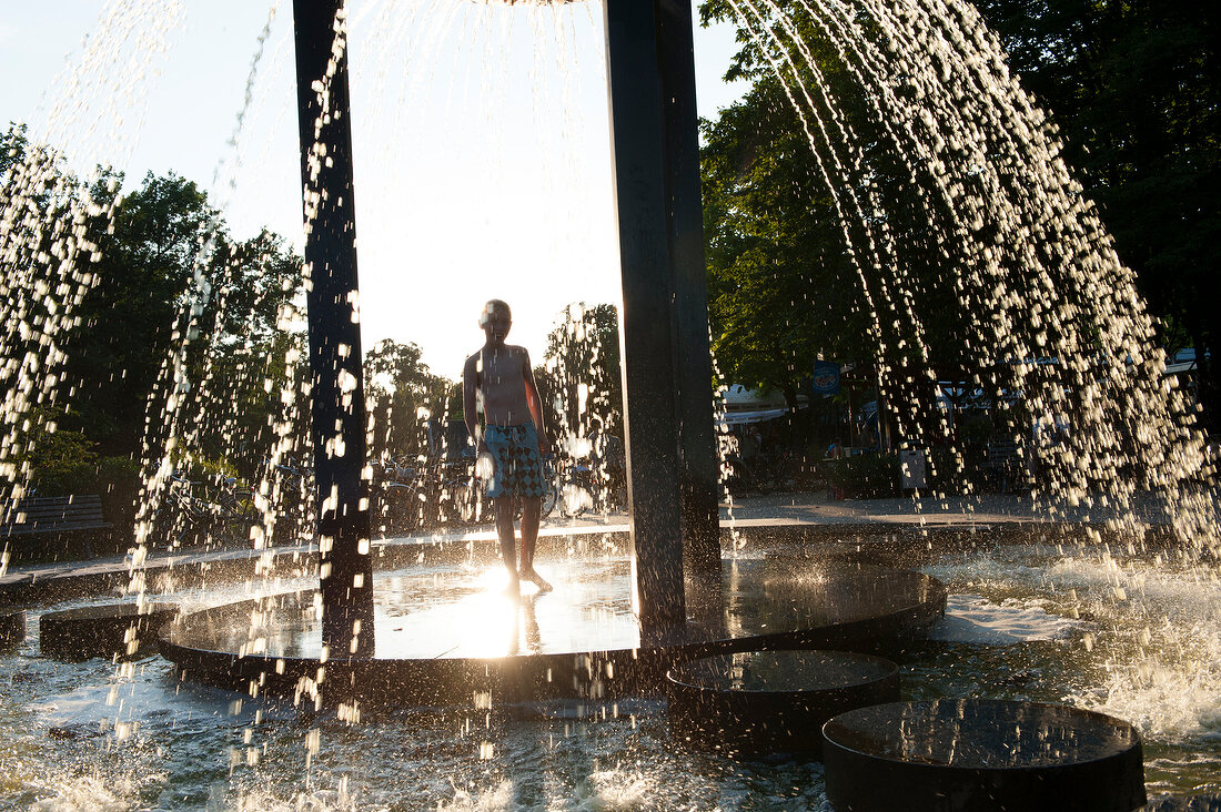 Man standing under water fountain at Friedrichshain public park in Berlin, Germany