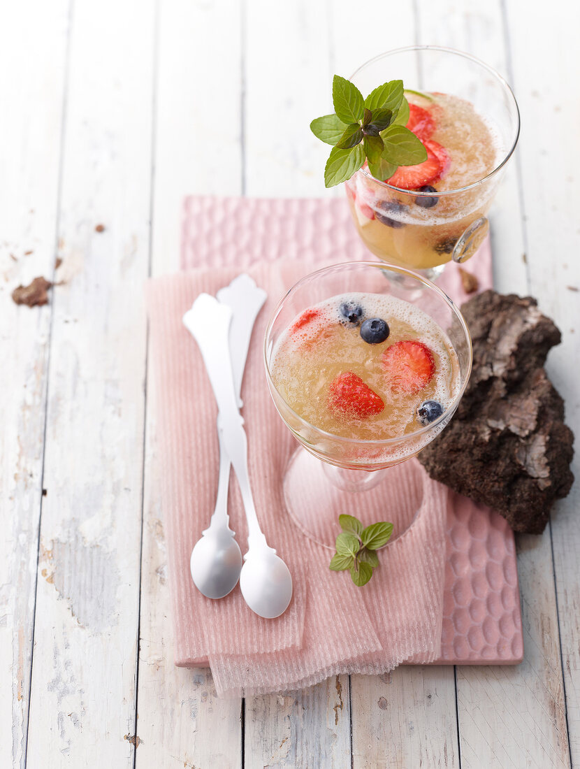 Two glass of elderflower and prosecco jelly with berries and mint next to dessert spoon