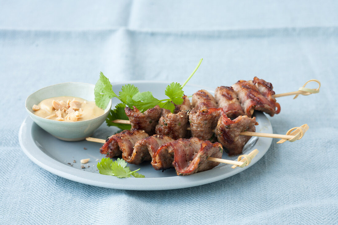 Bowl of peanut sauce served with meat satay skewers on plate