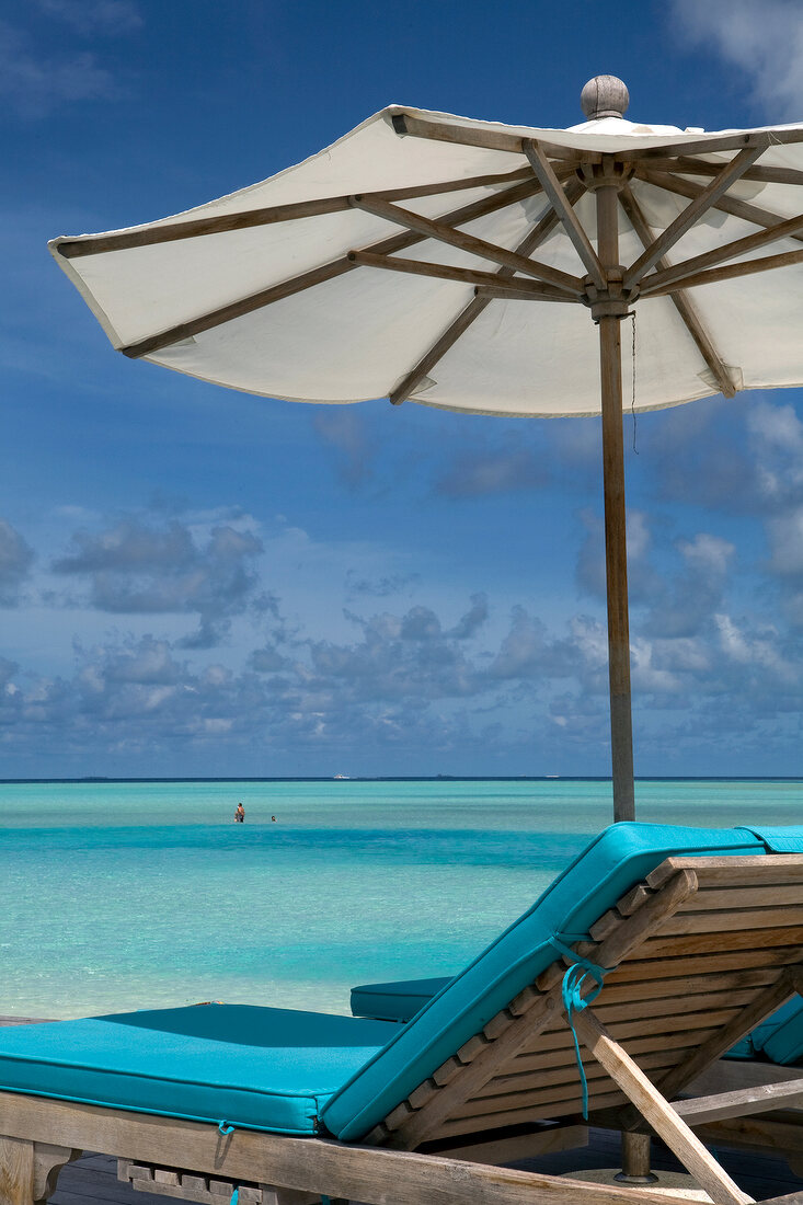 View of footbridge with umbrella and two women in sea, Anantara Dhigu island, Maldives