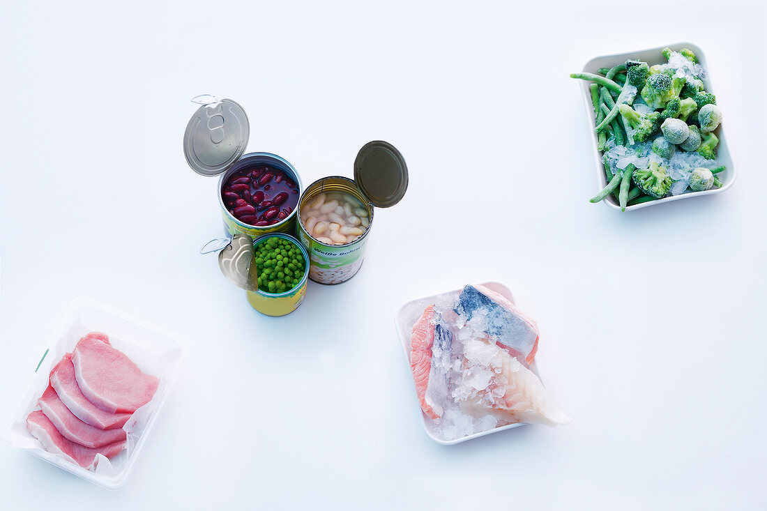 Vegetables, fish, meat in bowls and beans in tin on white background