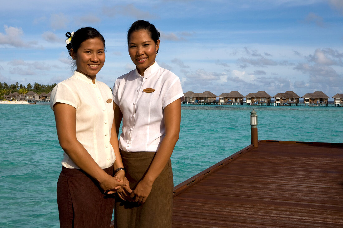 Two women standing on deck and Dhigufinolhu bungalows in water at dock in Maldives island