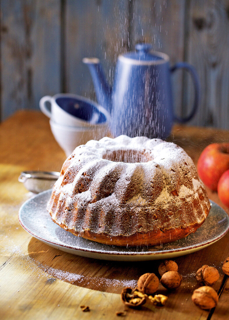Bundt cake with icing sugar and walnuts on plate