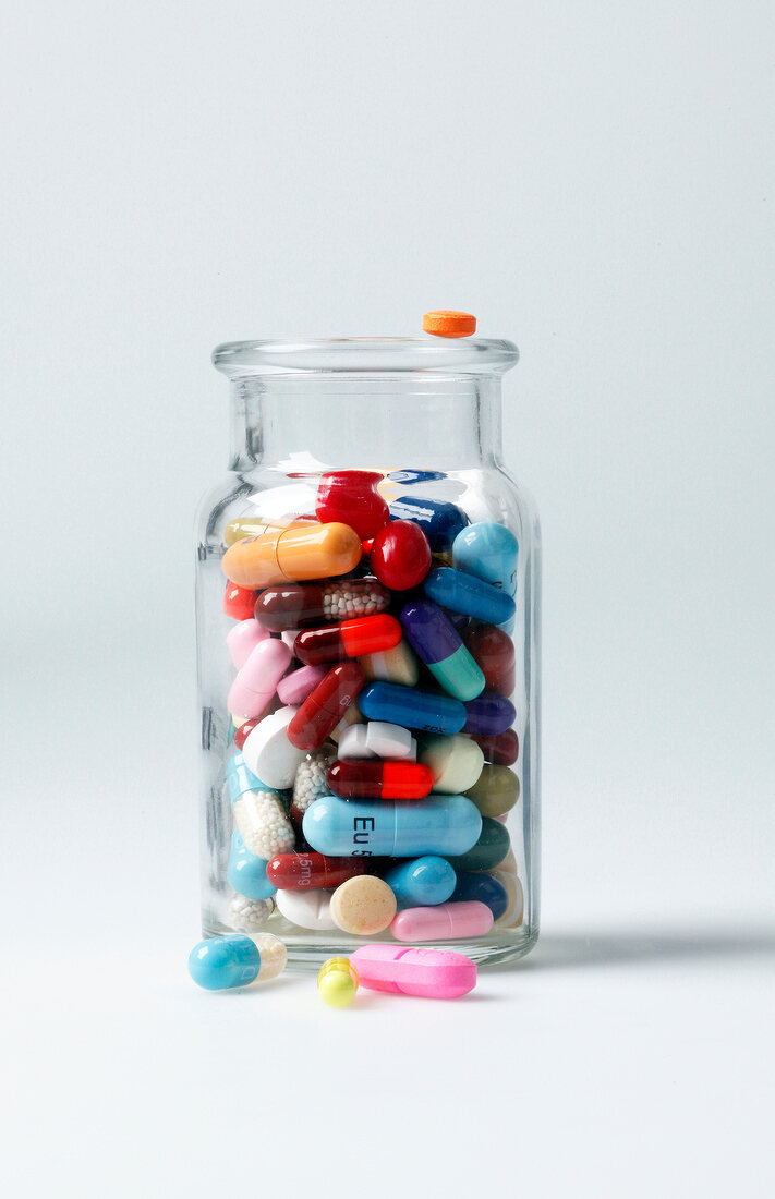 Close-up of glass jar with colourful tablets on white background