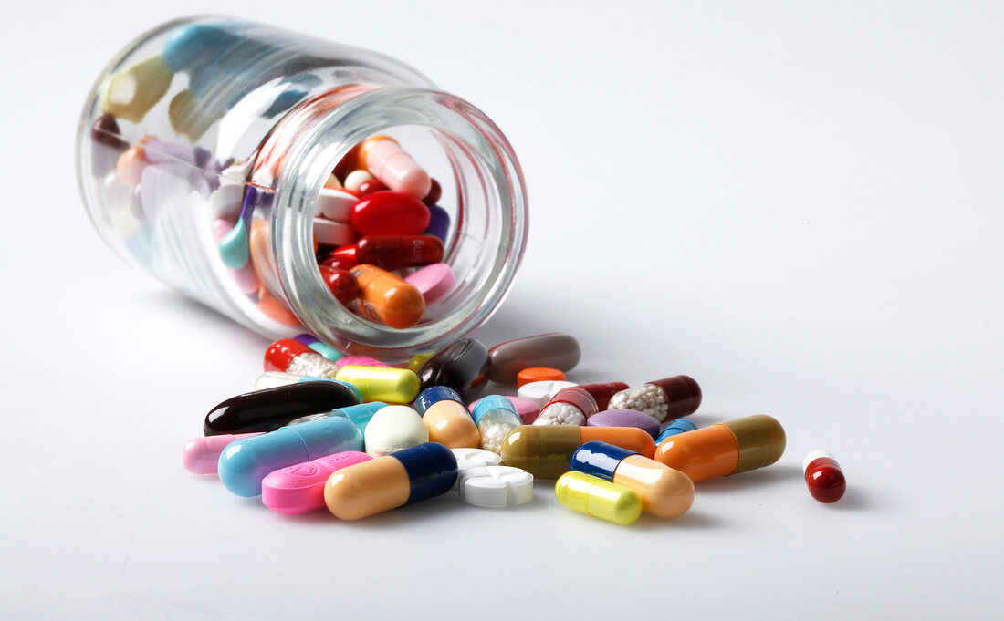 Close-up of glass jar with colourful tablets spilled on white background