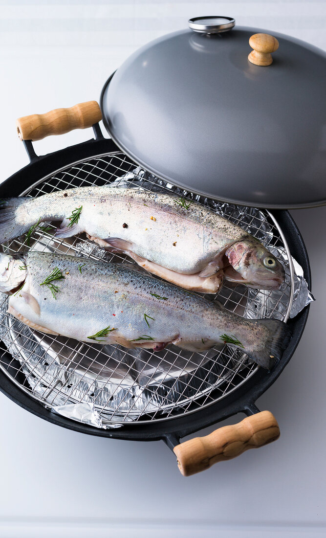 Trout sprinkled with herbs on grill in wok