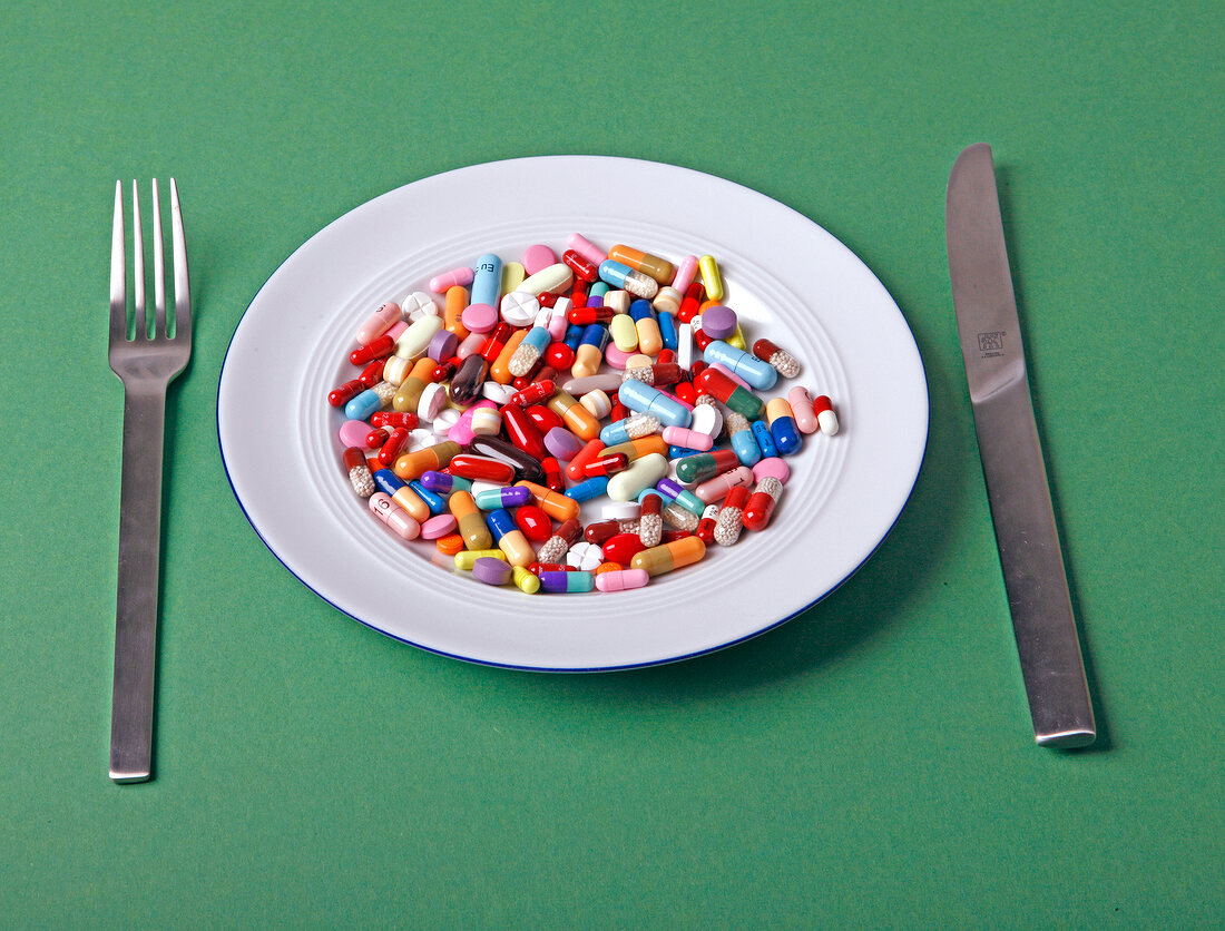 Various colourful tablets kept on plate with knife and fork next to it on green background