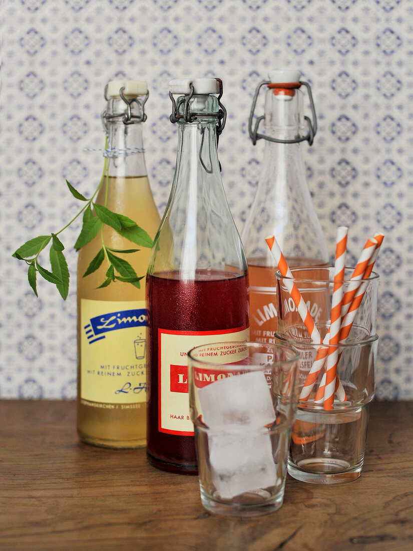 Bottles of three soft drinks with ice cubes and straw