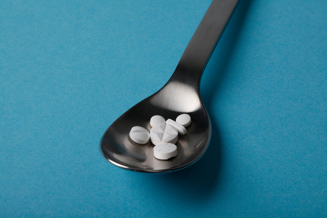 Close-up of spoon with tablets on blue background