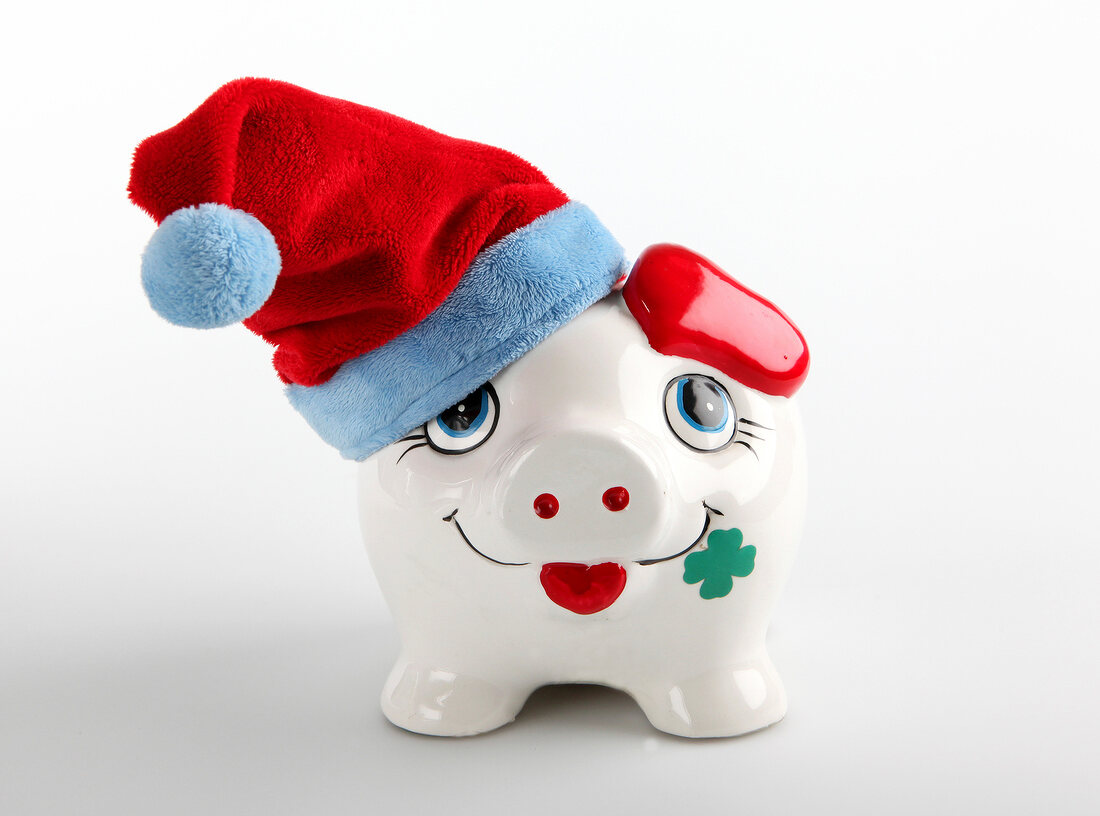 Close-up of piggy bank with red head warmer against white background