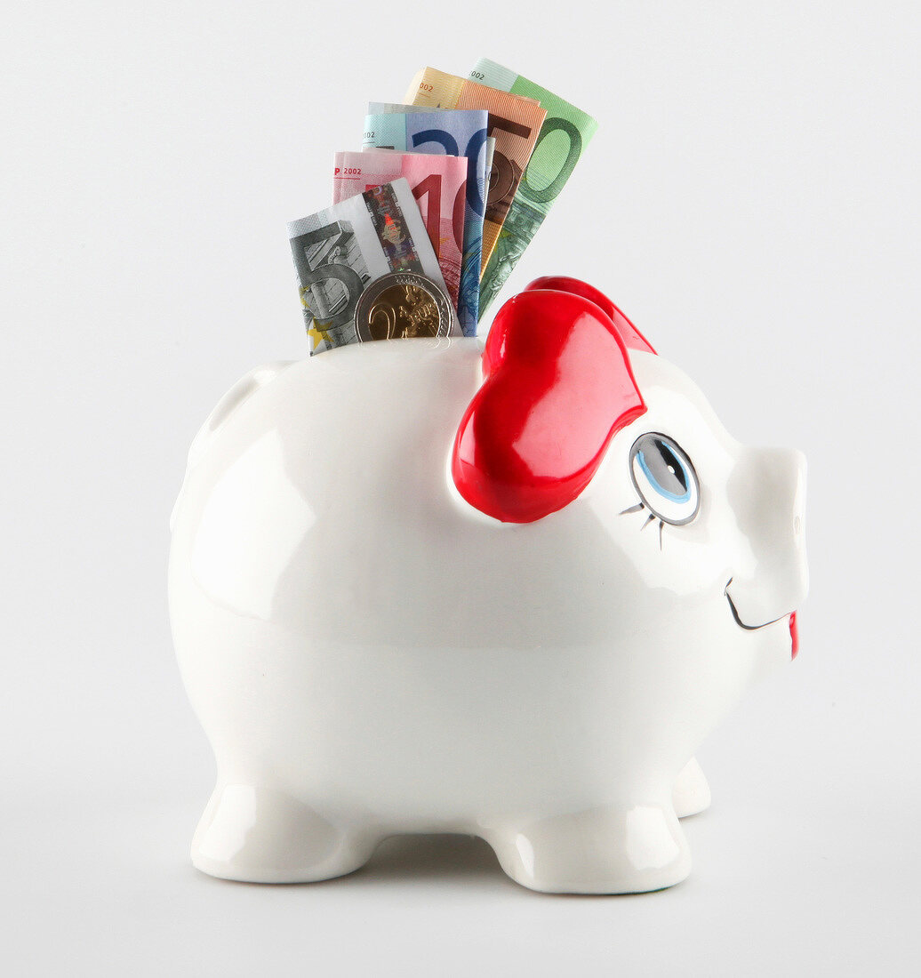 Close-up of white piggy bank with heart shaped ears and euro currencies