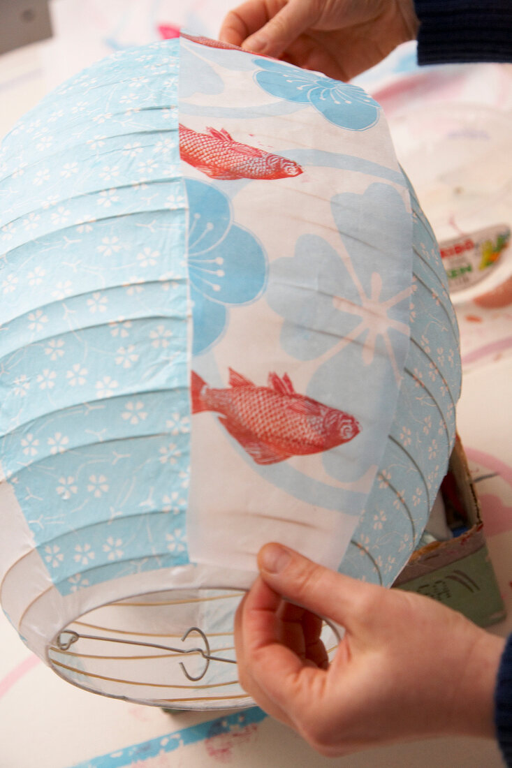 Close-up of person painting colourful lantern with flower and fish motif