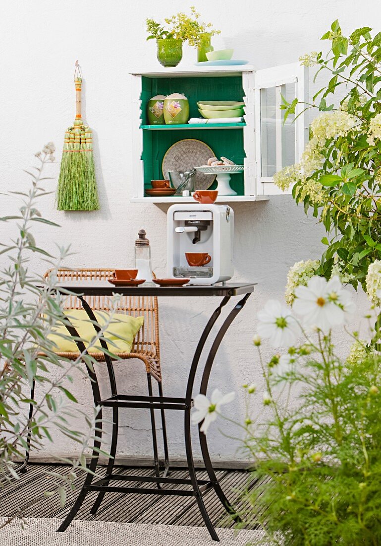 Crockery in small, wall-mounted cabinet above espresso machine on table on balcony