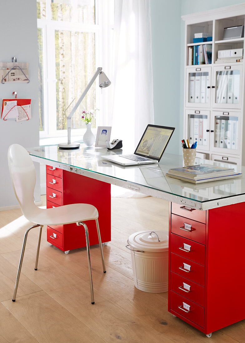 Office desk in red with table lamp, laptop and chair