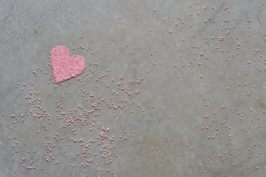 Pink sugar pearls and heart on gray background