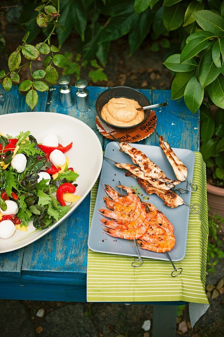 Mango salad with mini mozzarella, chicken satay, prawn skewers and a dip on a table outside