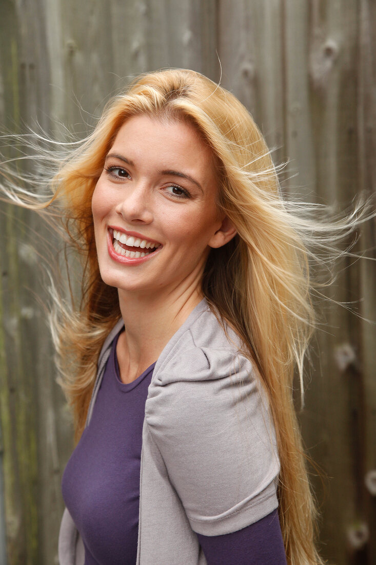 Portrait of beautiful blonde woman with long hair wearing purple top, smiling