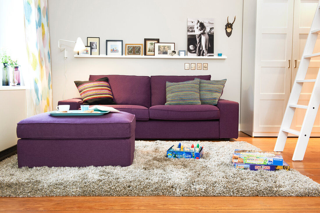 Living room with purple sofa, pouf, ladder and picture frames on wall