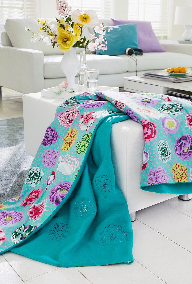 Living room with white sofa & floral blanket on pouffe