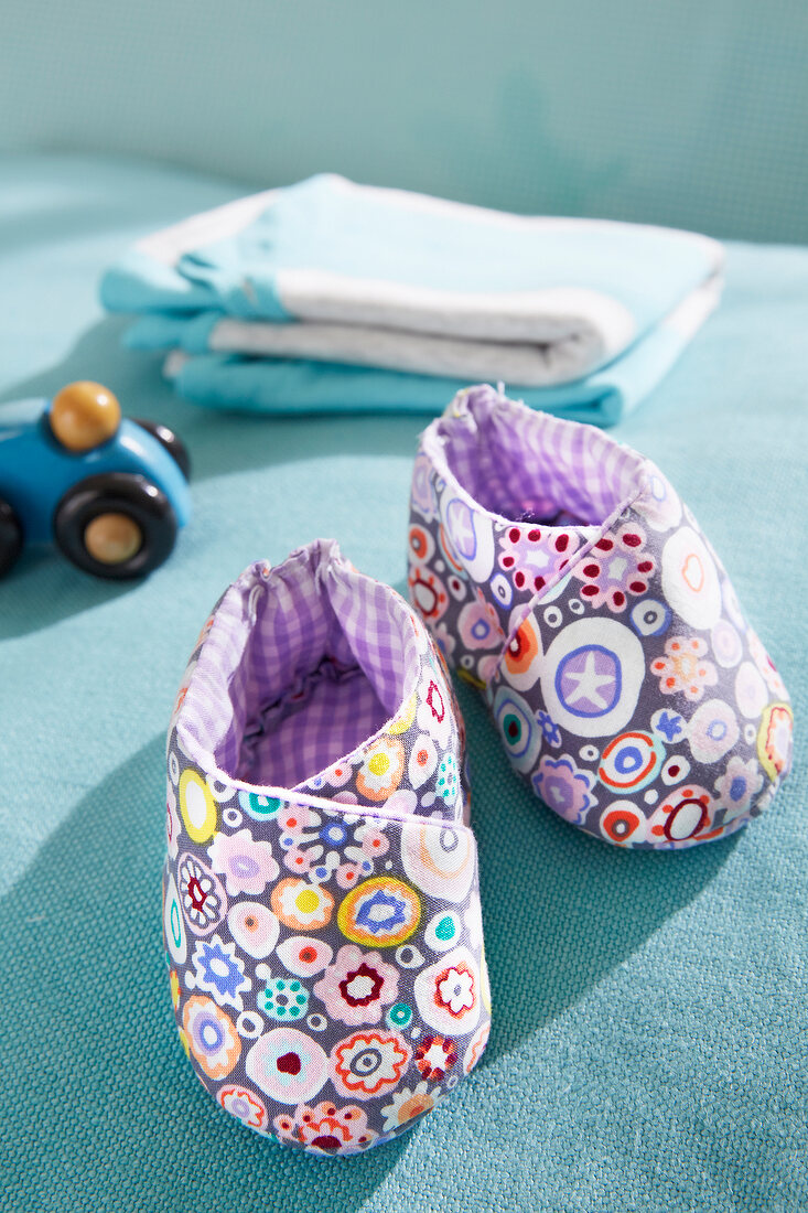 Purple homemade baby booties with flower motif on blue surface