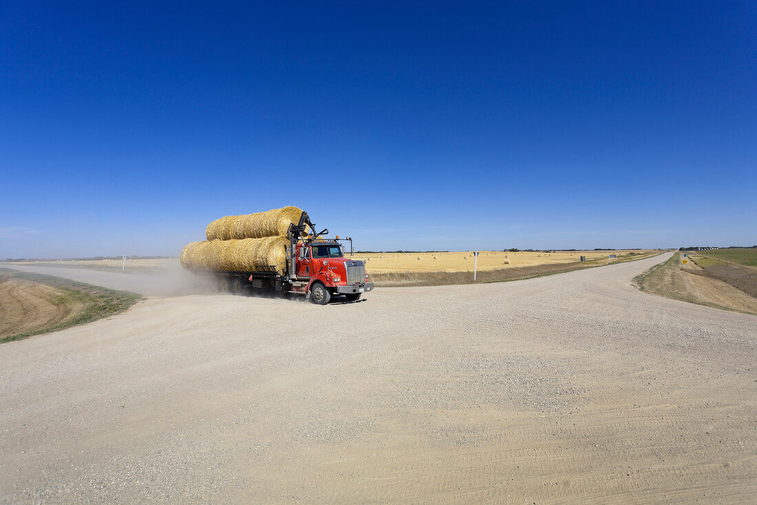 View of truck crossing the road 731 with bales of straw on road, Saskatchewan, Canada