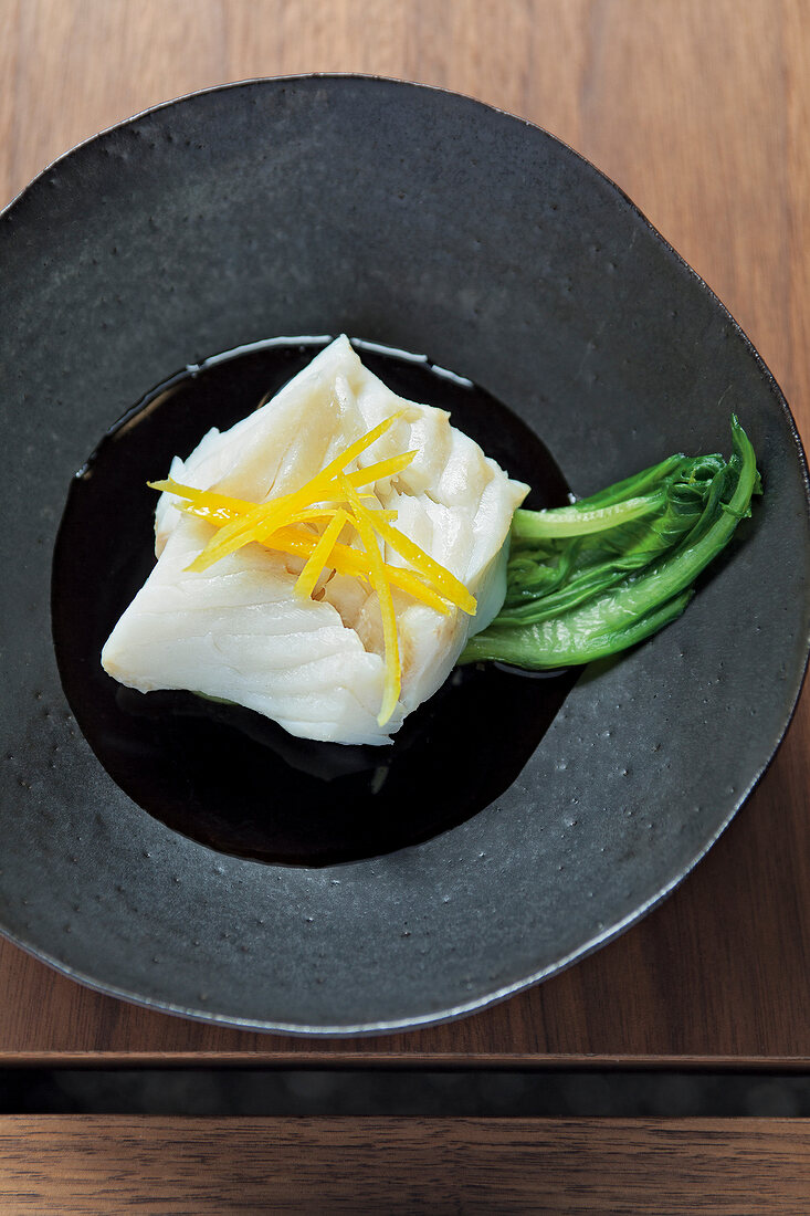Steamed cod with pak choi topped with lemon strips on plate