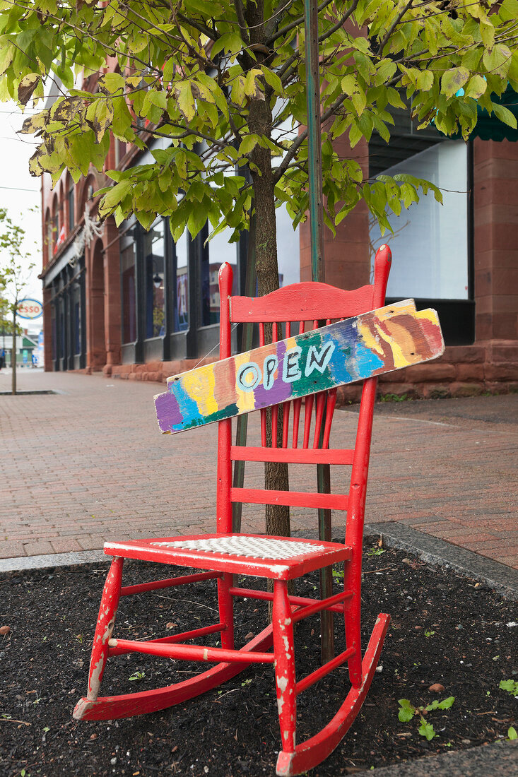 Red rocking chair with board open on it at pavement, Nova Scotia, Canada