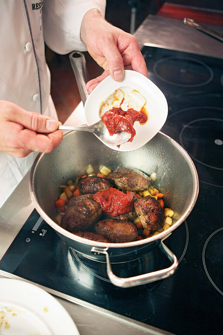 Close-up of chef adding ingredients in braised pork cheeks with vegetables