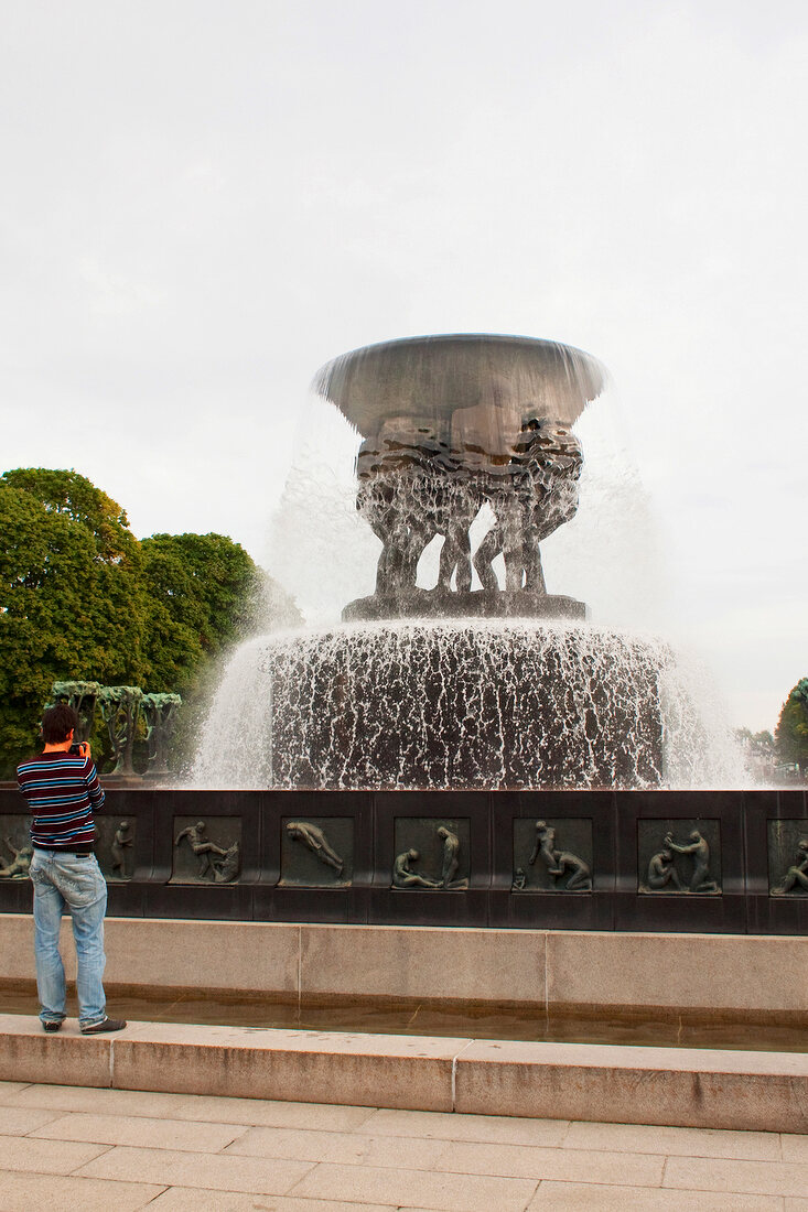 Man standing near the fountain with statues in Vigeland Sculpture park in Oslo, Norway