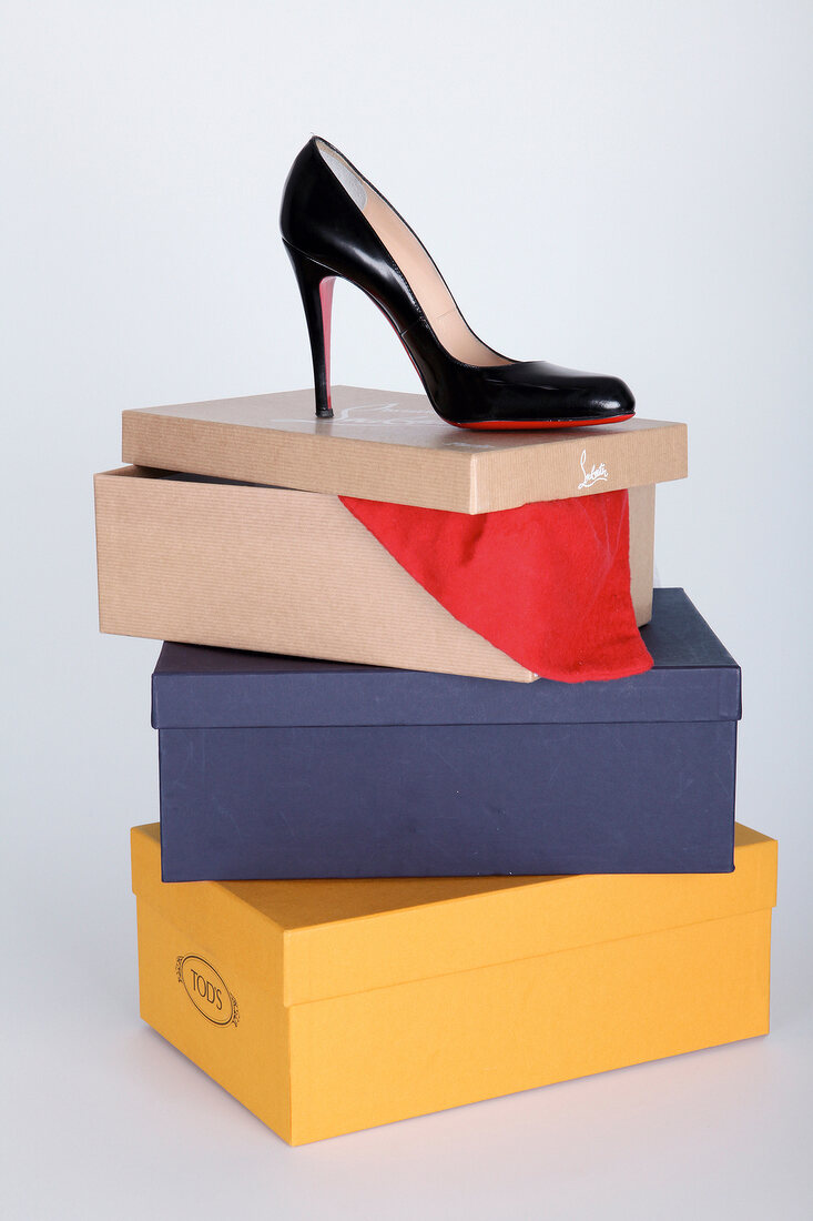 Black pump heel on stack of multi-coloured boxes against white background