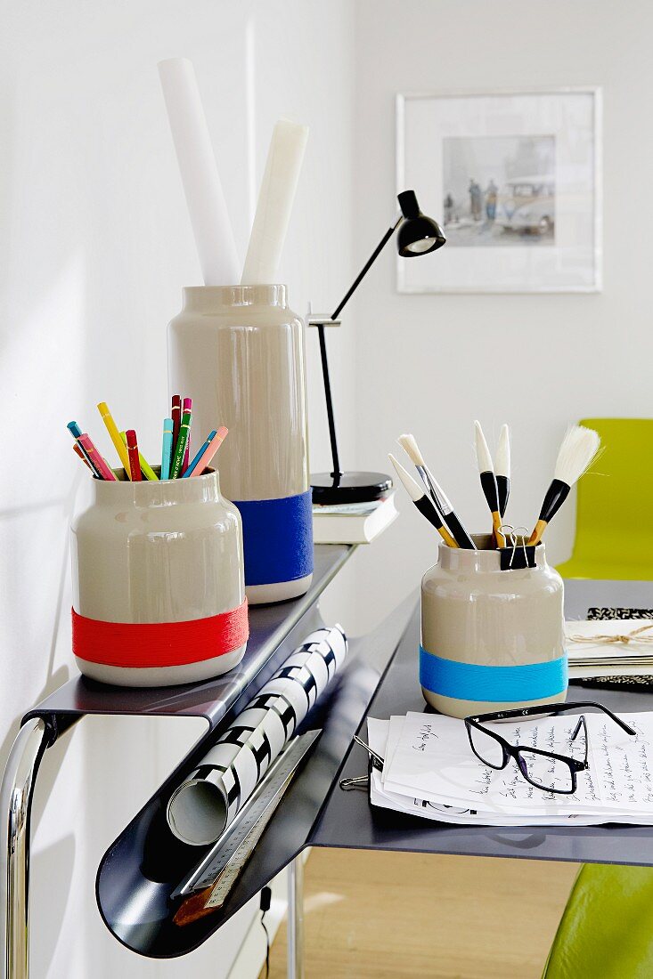 Plain grey vases decorated with stripes and used to store office supplies