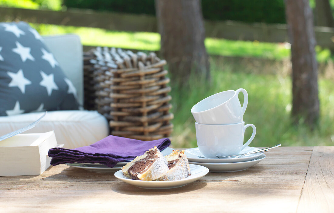 Cups, napkins and books on wooden table in garden