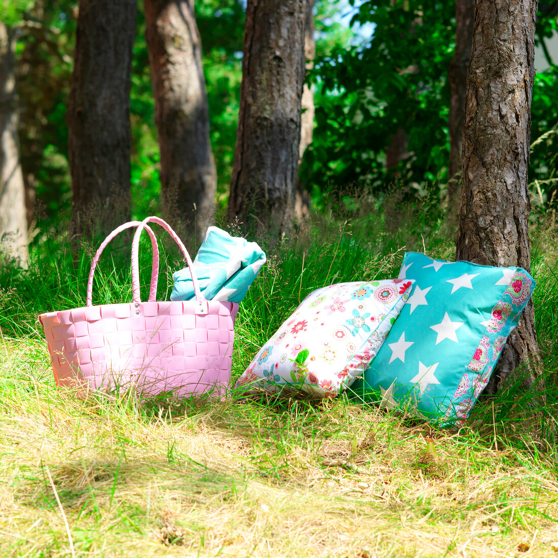Colourful pillows with pink wicker basket under tree in garden