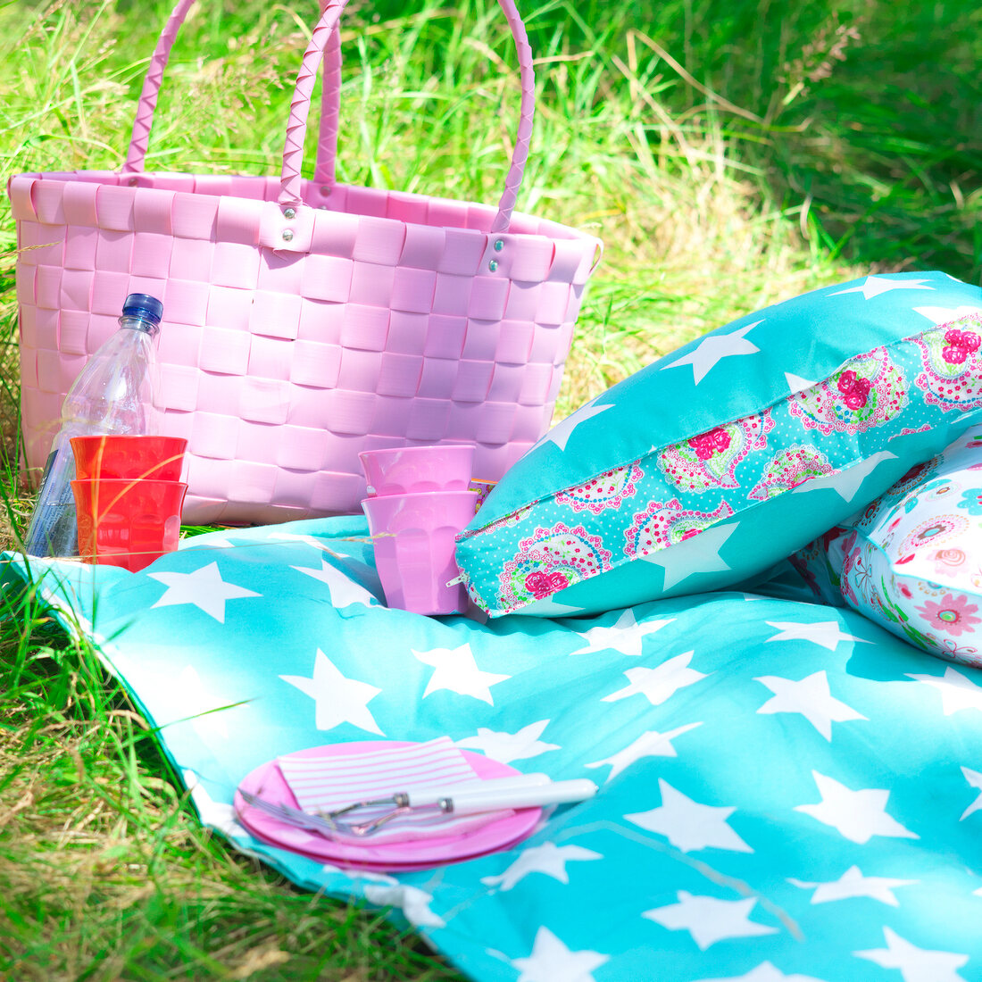 Colourful cushions and blanket with pink wicker basket in garden