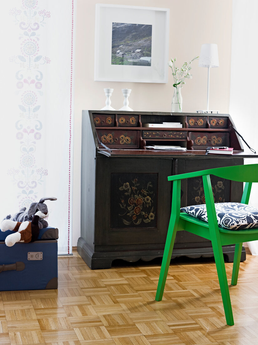 Antique table with flower vase and green chair with cushion by side