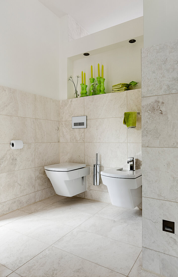 Bathroom with white toilet seat, bidet and wall shelf with green accessories