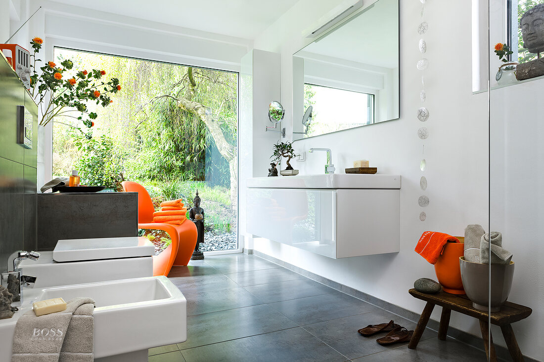 Luxurious bathroom with sink, large windows and orange accessories