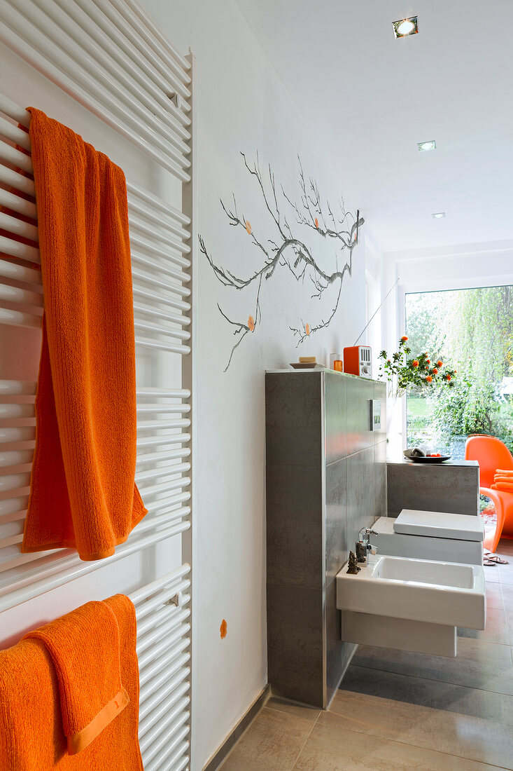 Interior of luxury bathroom with toilet seat, bidet and orange towels on radiator