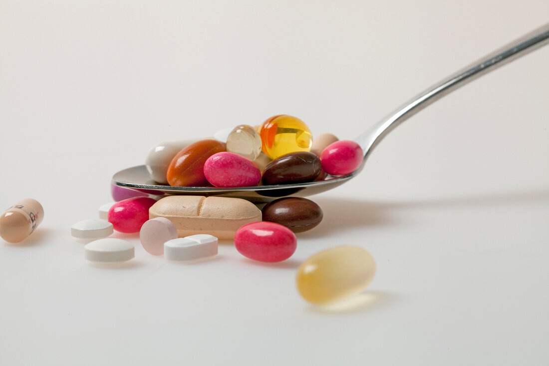 Close-up of pills, tablets, dragees and capsules in spoon against white background